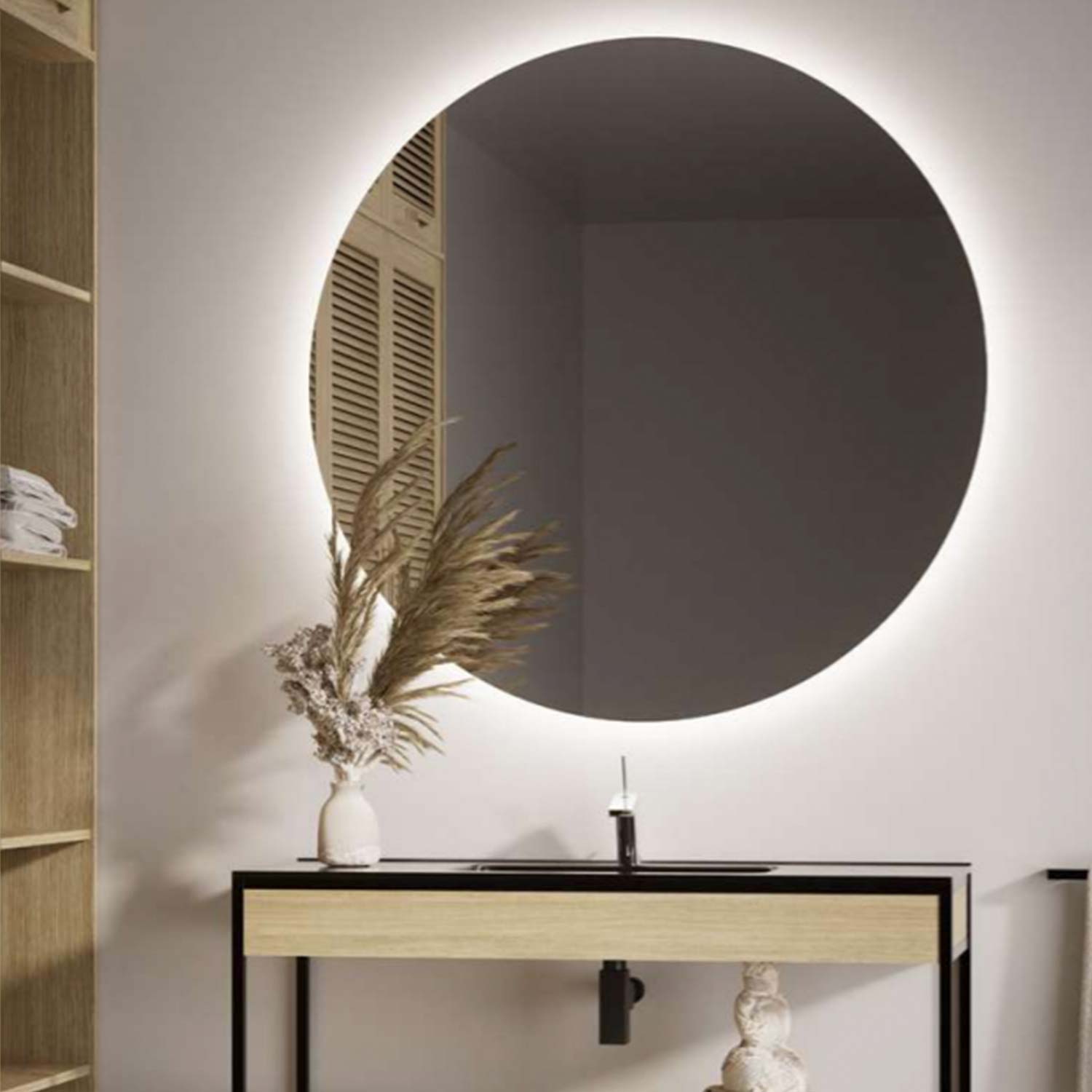 Round mirror on a wall with a minimalistic setup including a vase and plant.