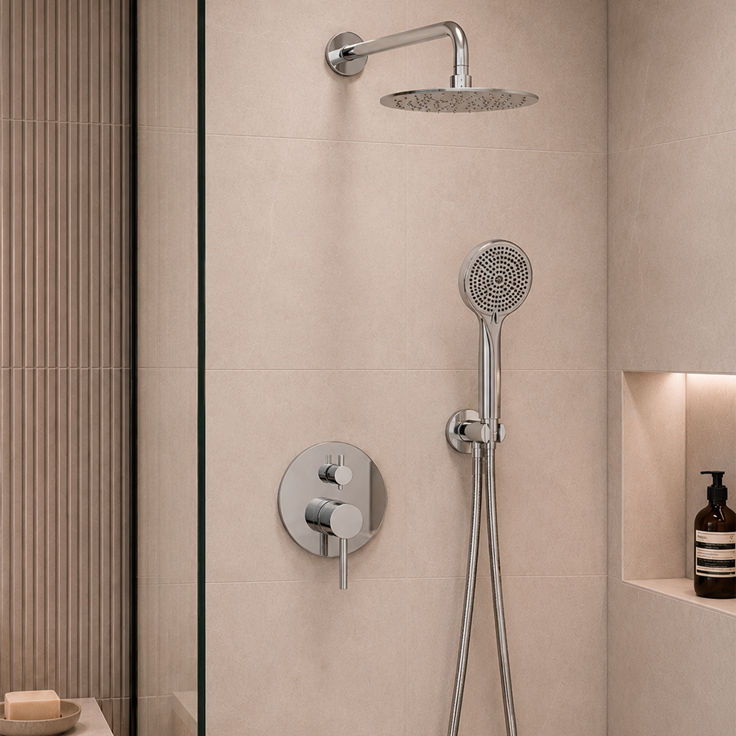 A modern wall-mounted shower system with a round rain shower head, handheld shower wand, and circular control valve plate in polished chrome, installed on beige tiled walls in a bathroom.