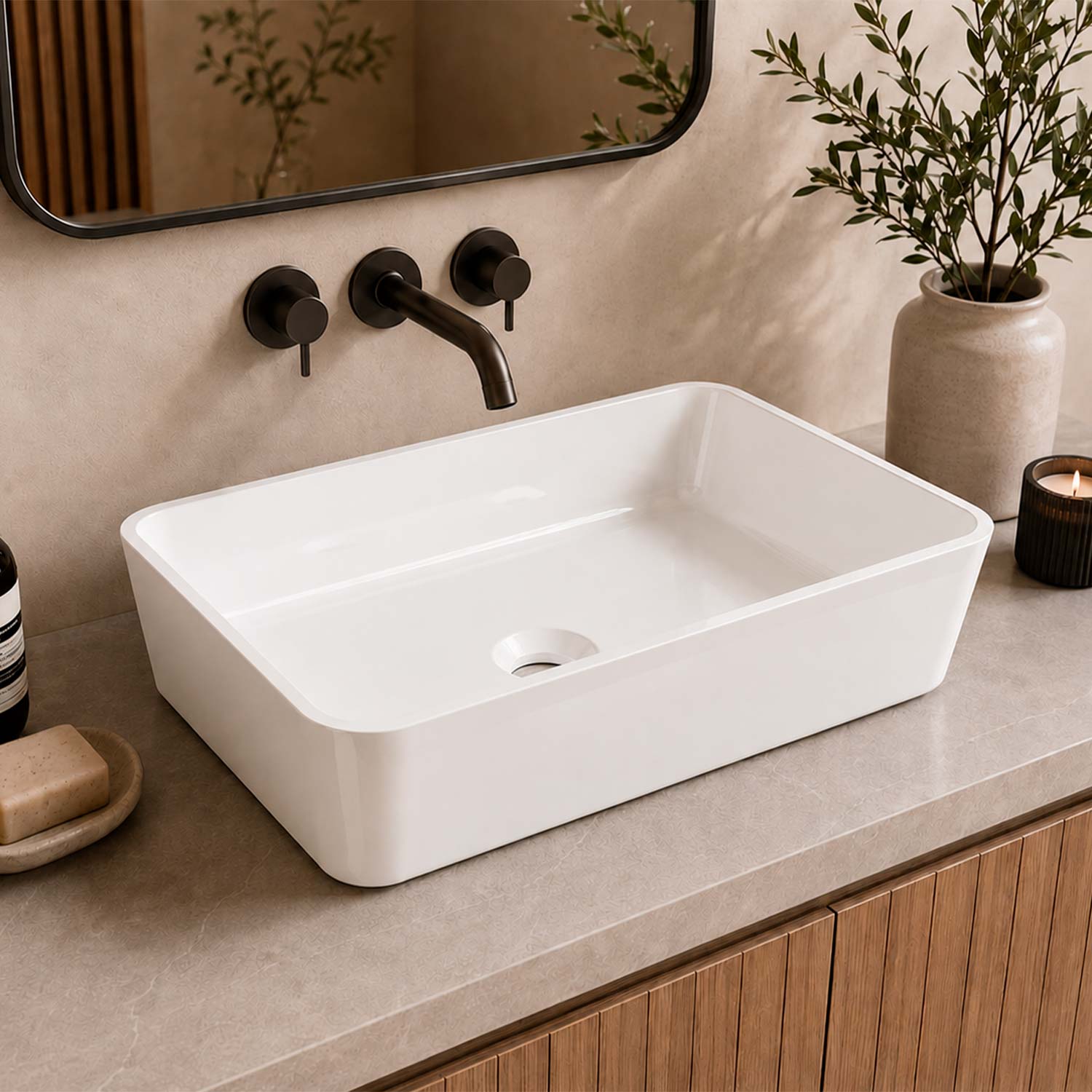 A white rectangular vessel sink basin installed on a beige stone countertop with a matte black wall-mounted faucet and controls, shown in a styled bathroom setting with a mirror, plant, soap dish, and candle.